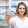 Selective focus of blister pack of pills, female pharmacist holding in hand. Professional specialist showing medicines. Blurred woman with short haircut looking at camera and smiling.