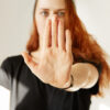 Close up view of young woman making stop gesture with her hand. Cropped isolated portrait of redhead female in cap and black T-shirt standing against white background. Selective focus, film effect